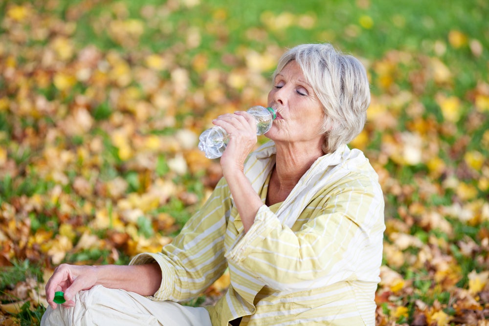 Ältere Dame leidet an Mundtrockenheit und trinkt Wasser in einem Park im Herbst