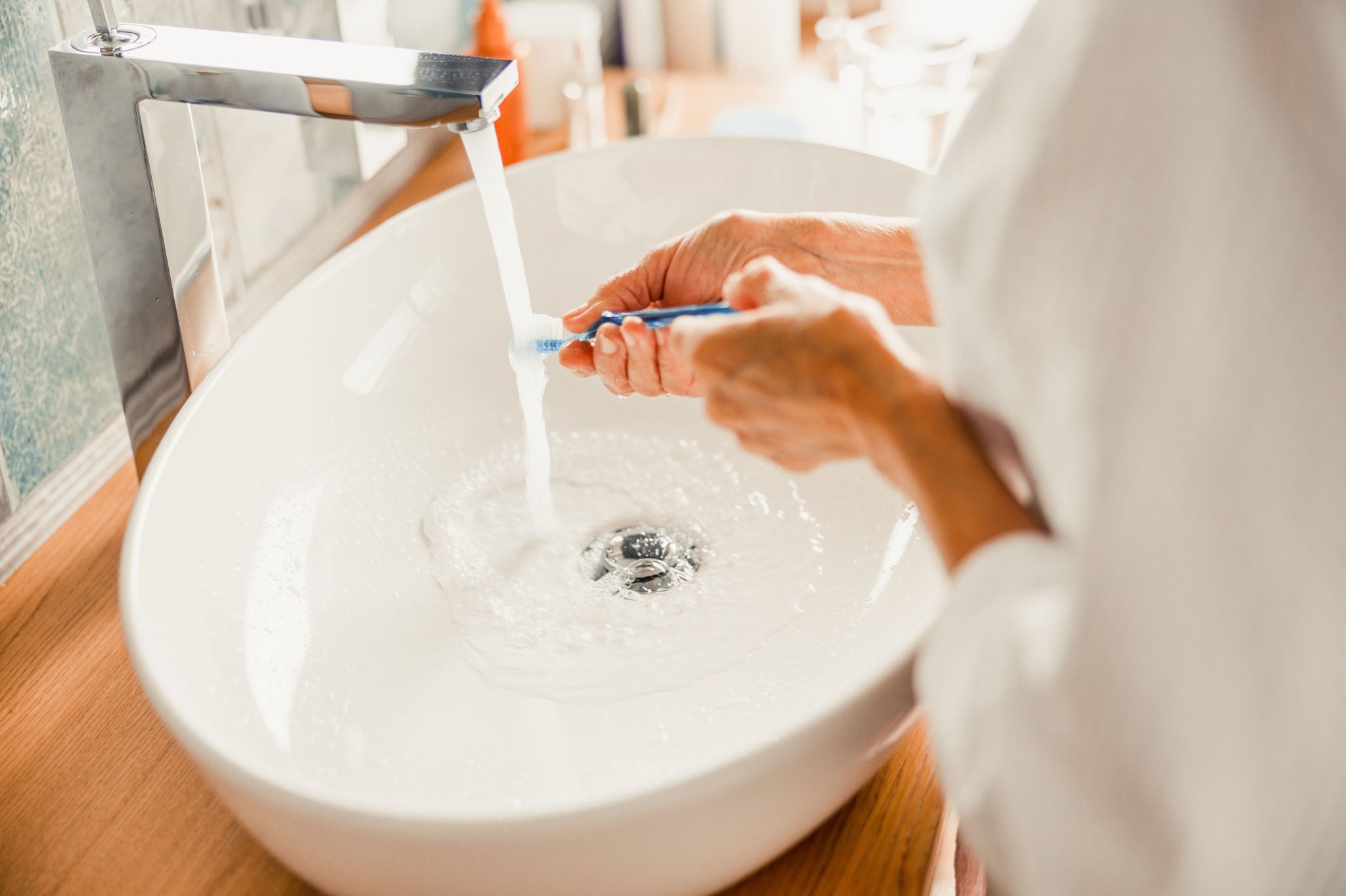 Close up of female hands holding toothbrush under running tap stock photo