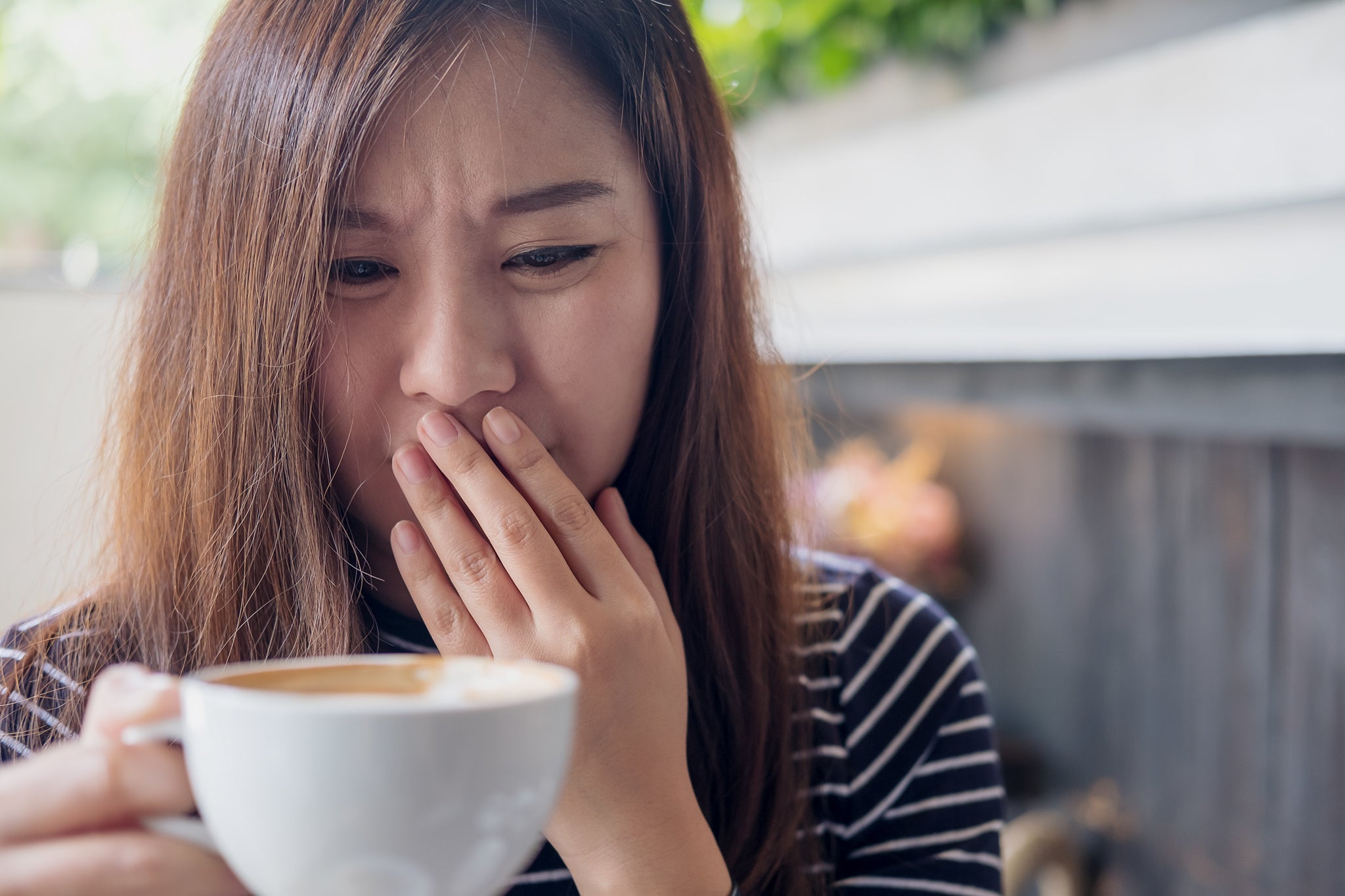 Asian woman drinking hot coffee cup outside hand over mouth