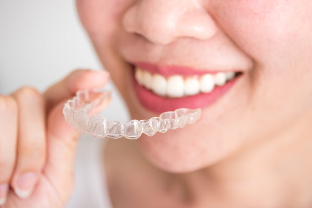 A smiling woman holding an invisalign braces or invisible retainer, orthodontic equipment