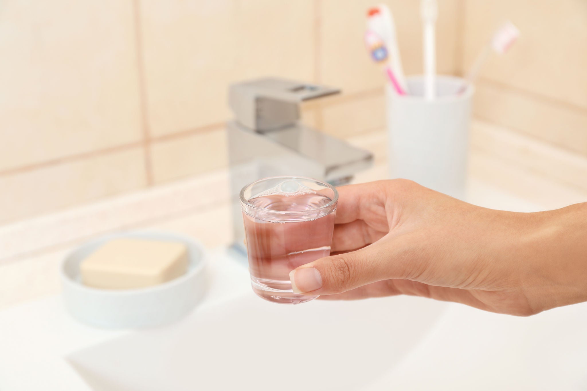 Woman holding glass with mouthwash for teeth and oral care in bathroom