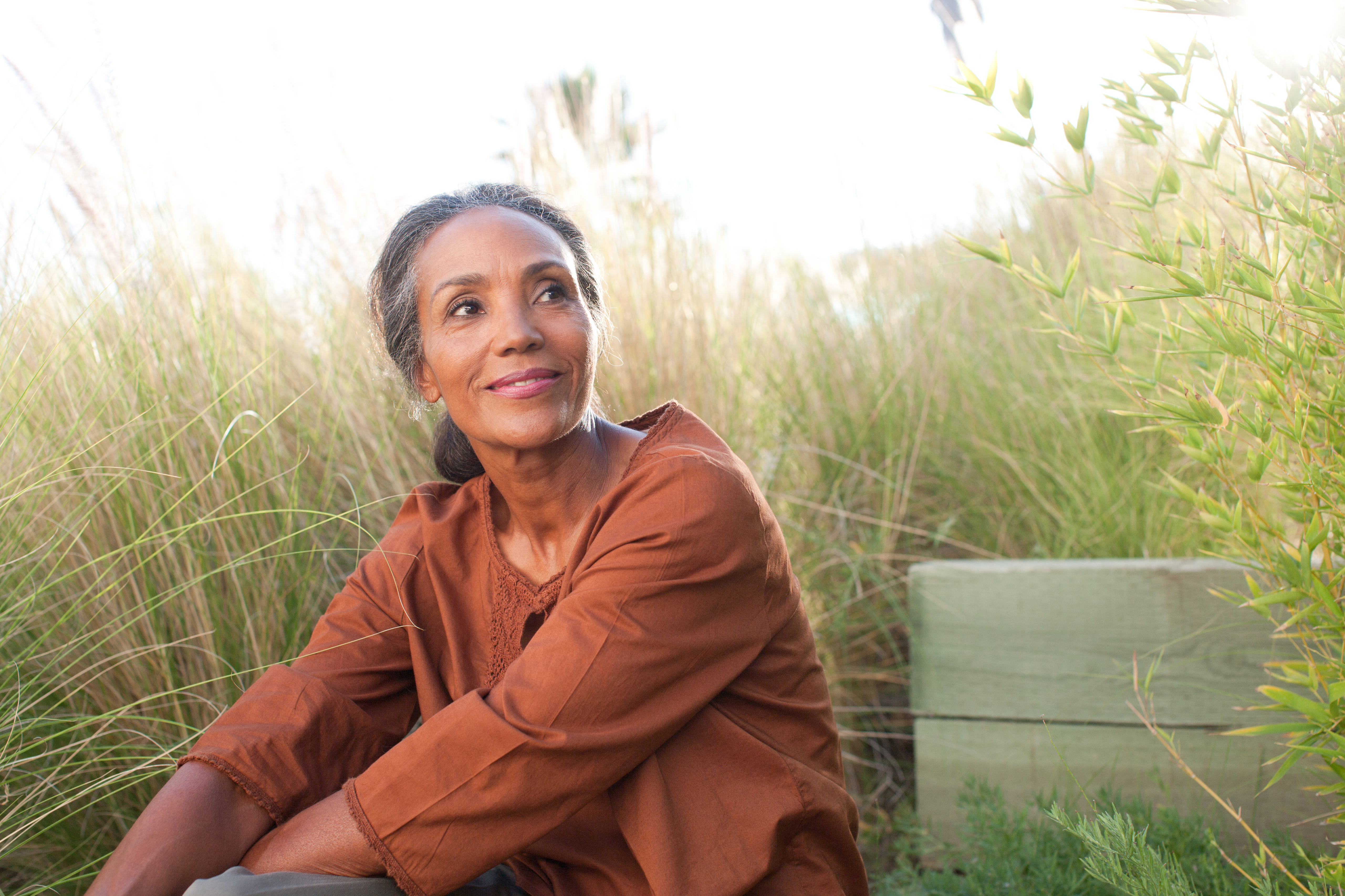 Black older woman sitting in green field, greying hair menopause