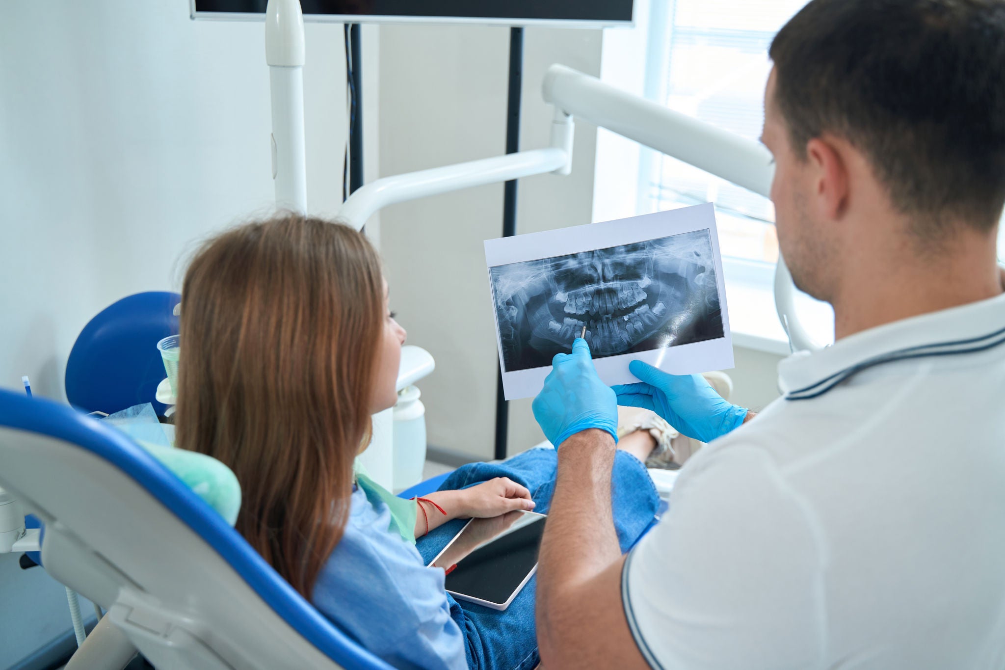 Qualified doctor showing carious cavity on panoramic x-ray to girl seated in chair
