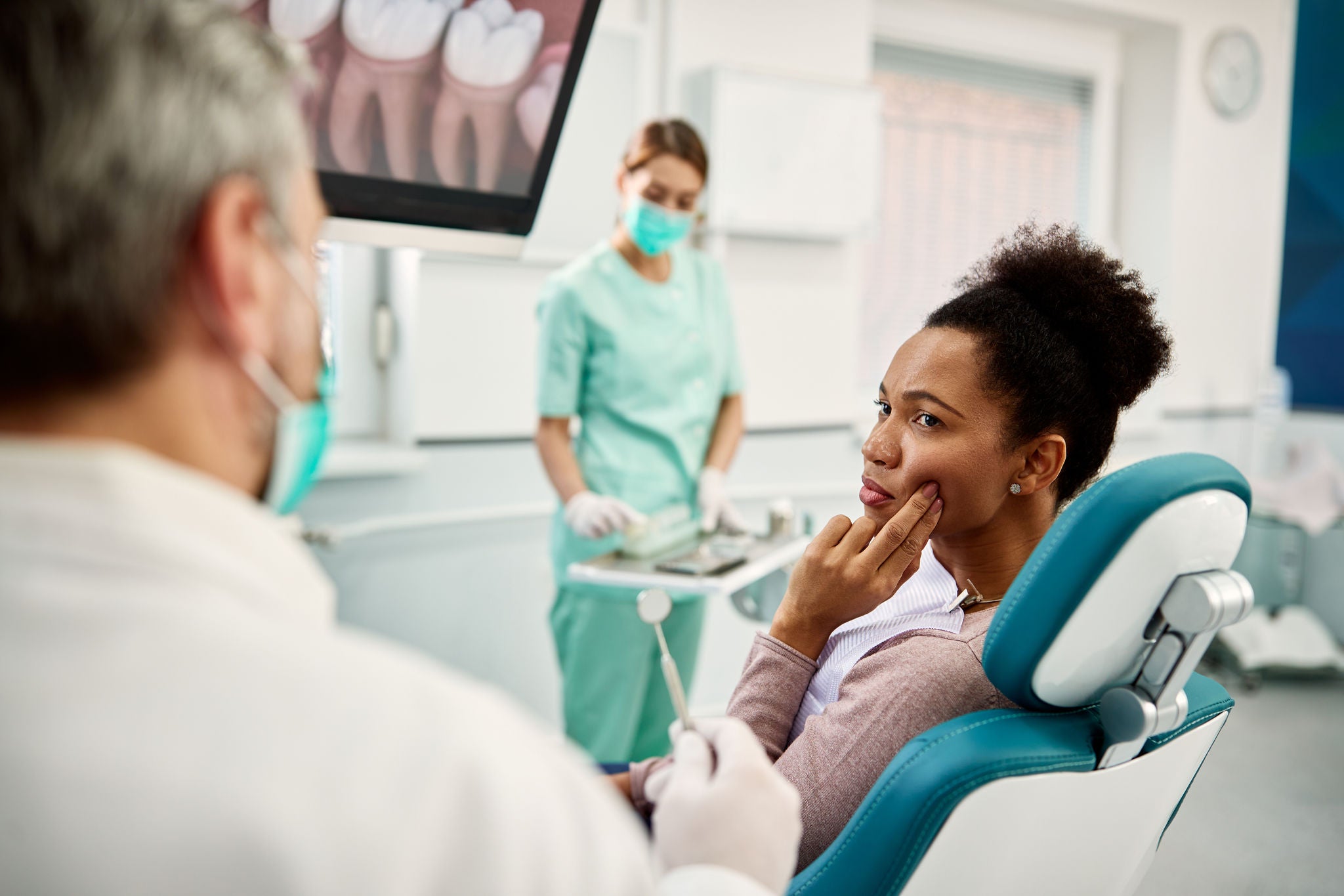 Black woman talking to a dentist and complaining about pain in her teeth during dental check-up at dentist's office.