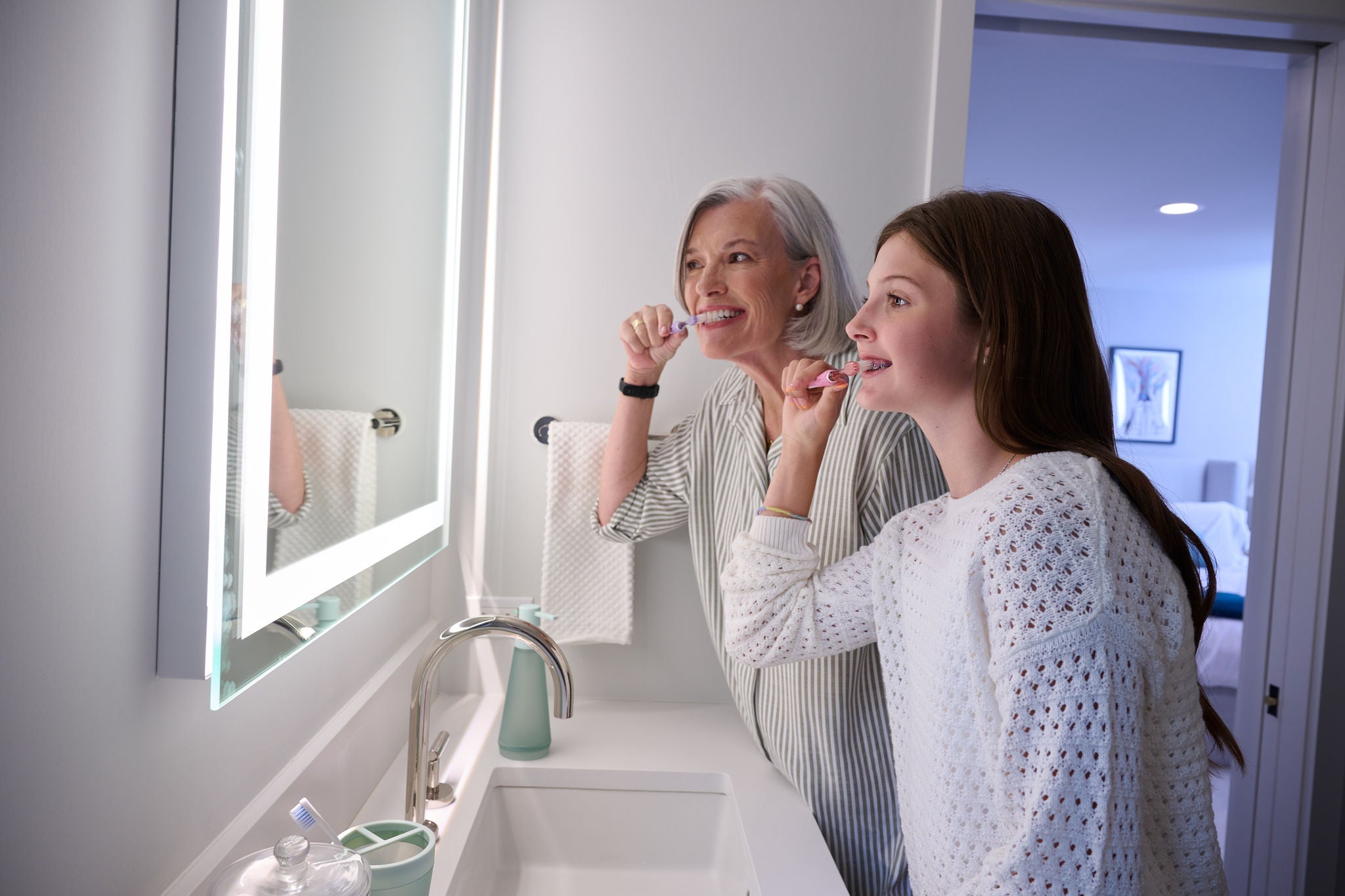 Senior woman and young girl brushing teeth with toothbrushes in a modern bathroom. Image resolution: 2048x1365.