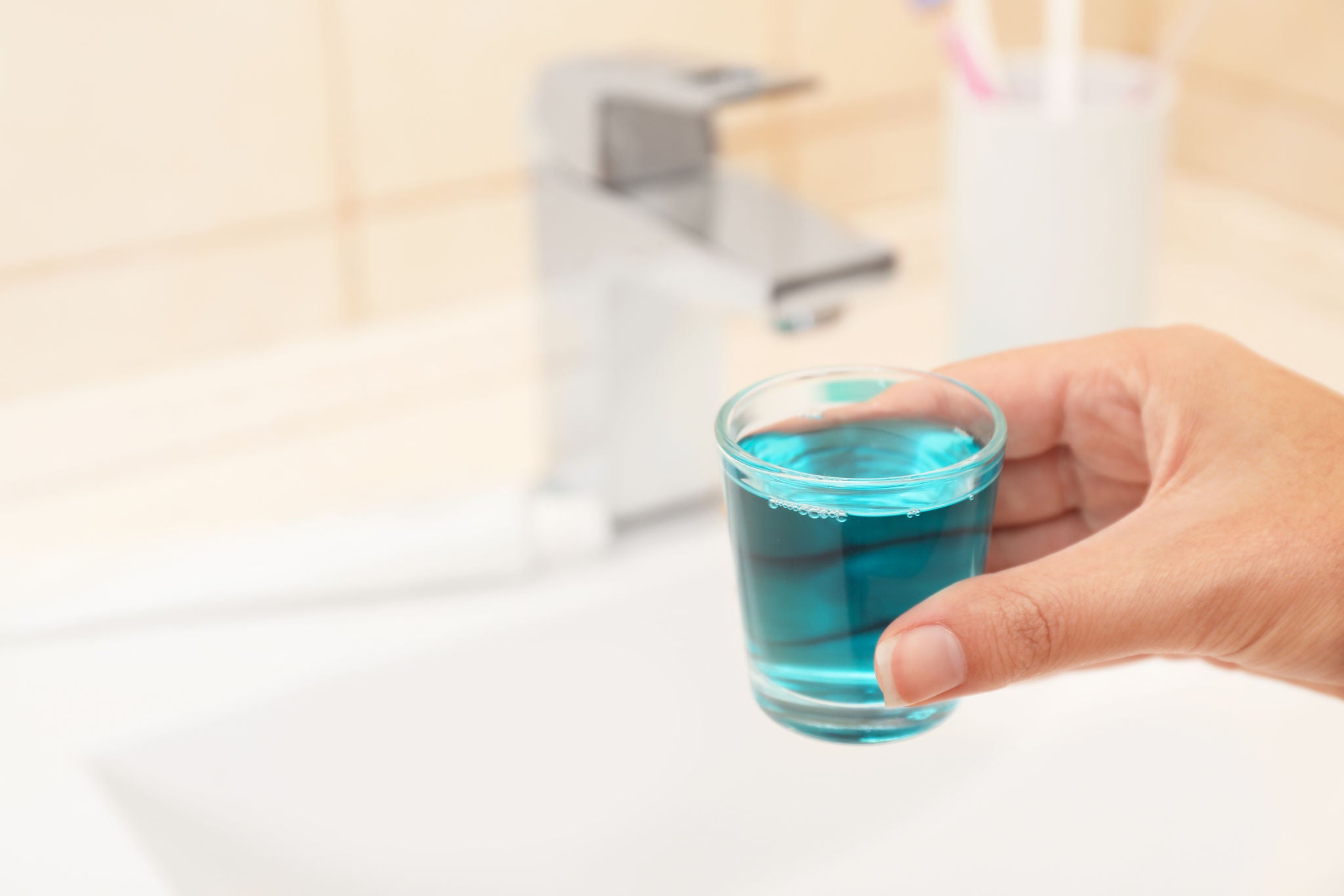 Woman holding glass with mouthwash for teeth and oral care in bathroom