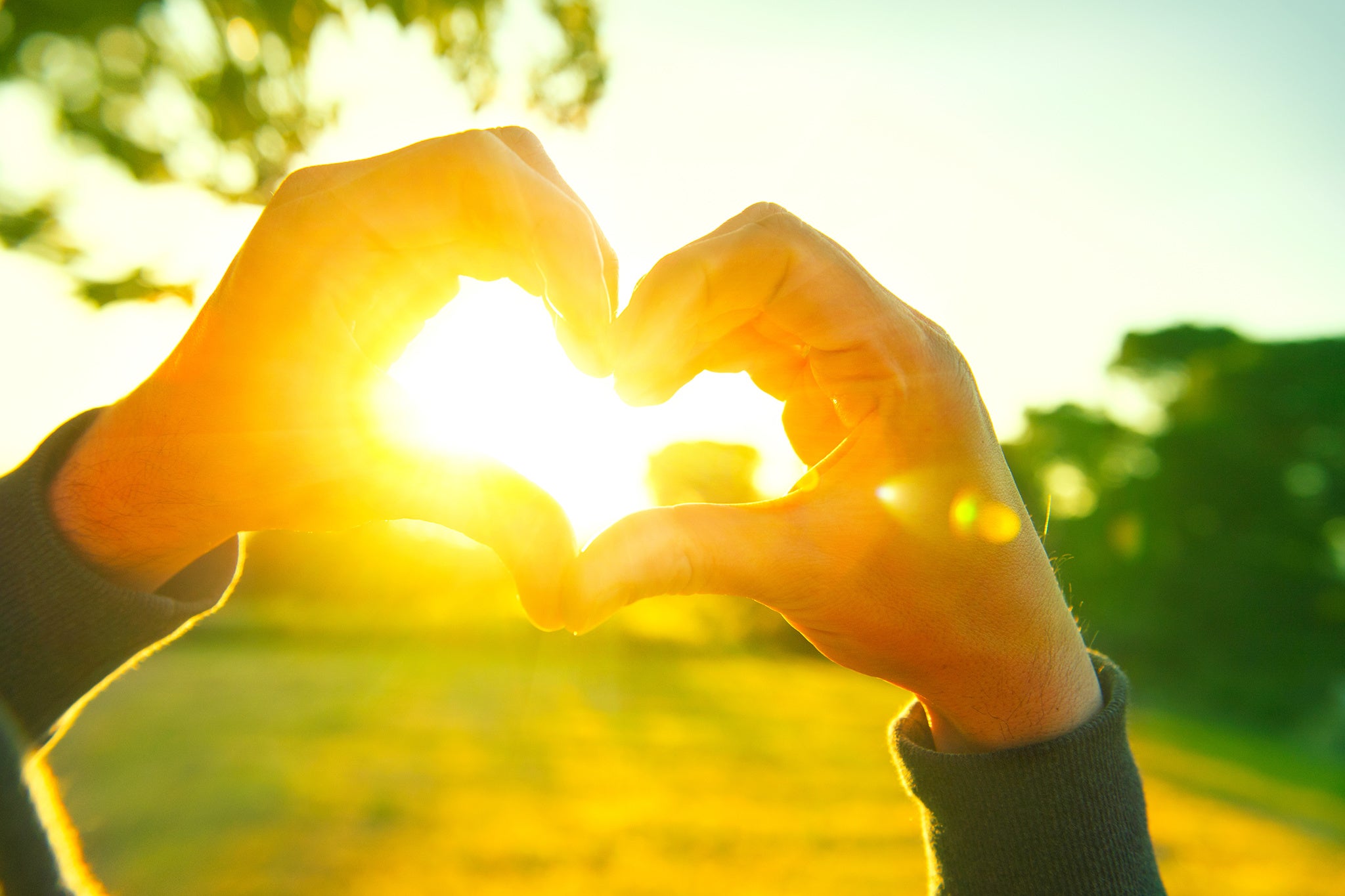 Shaping a heart with hands outside sunset