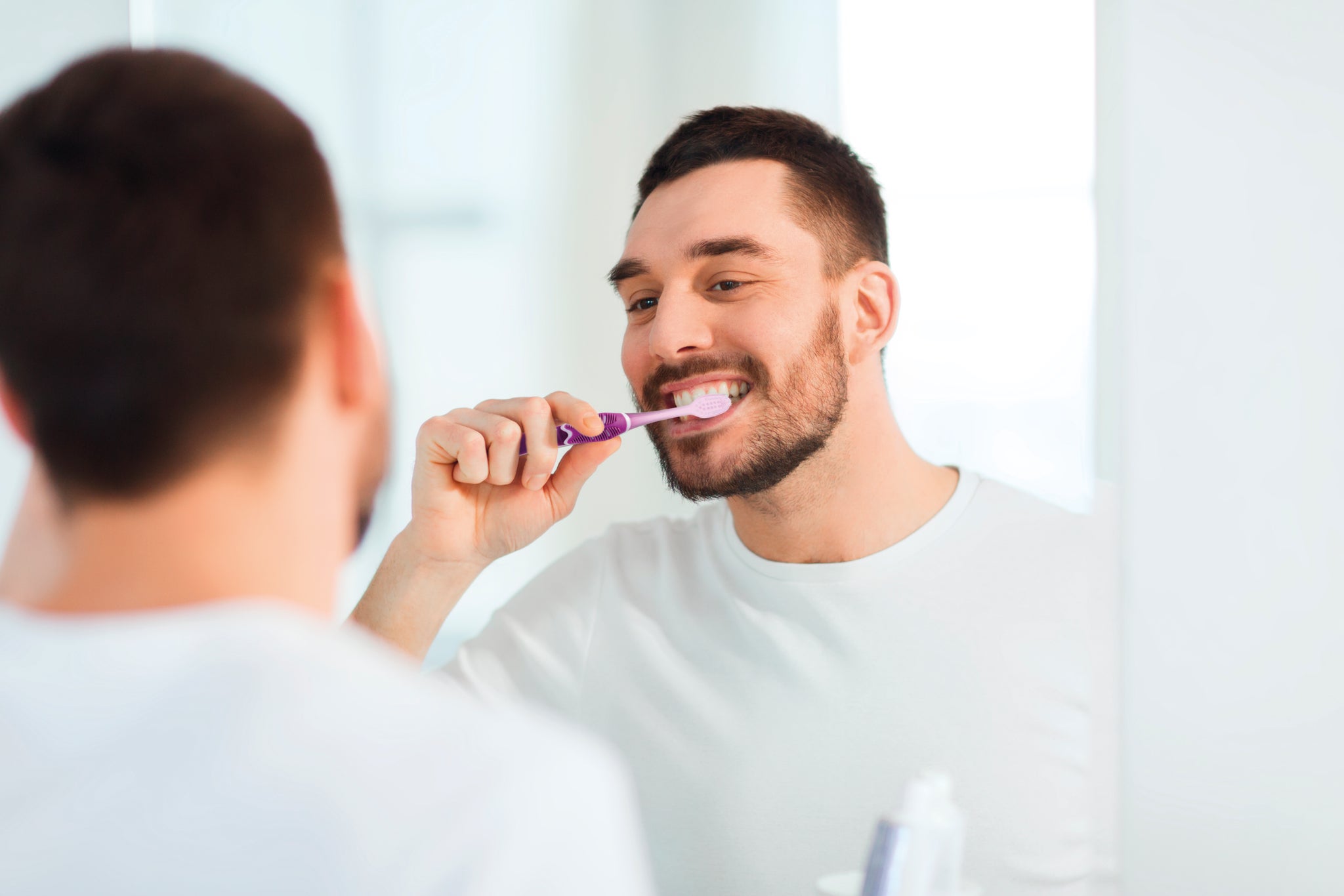 Young man brushing his teeth in front of a bathroom mirror technique pro purple