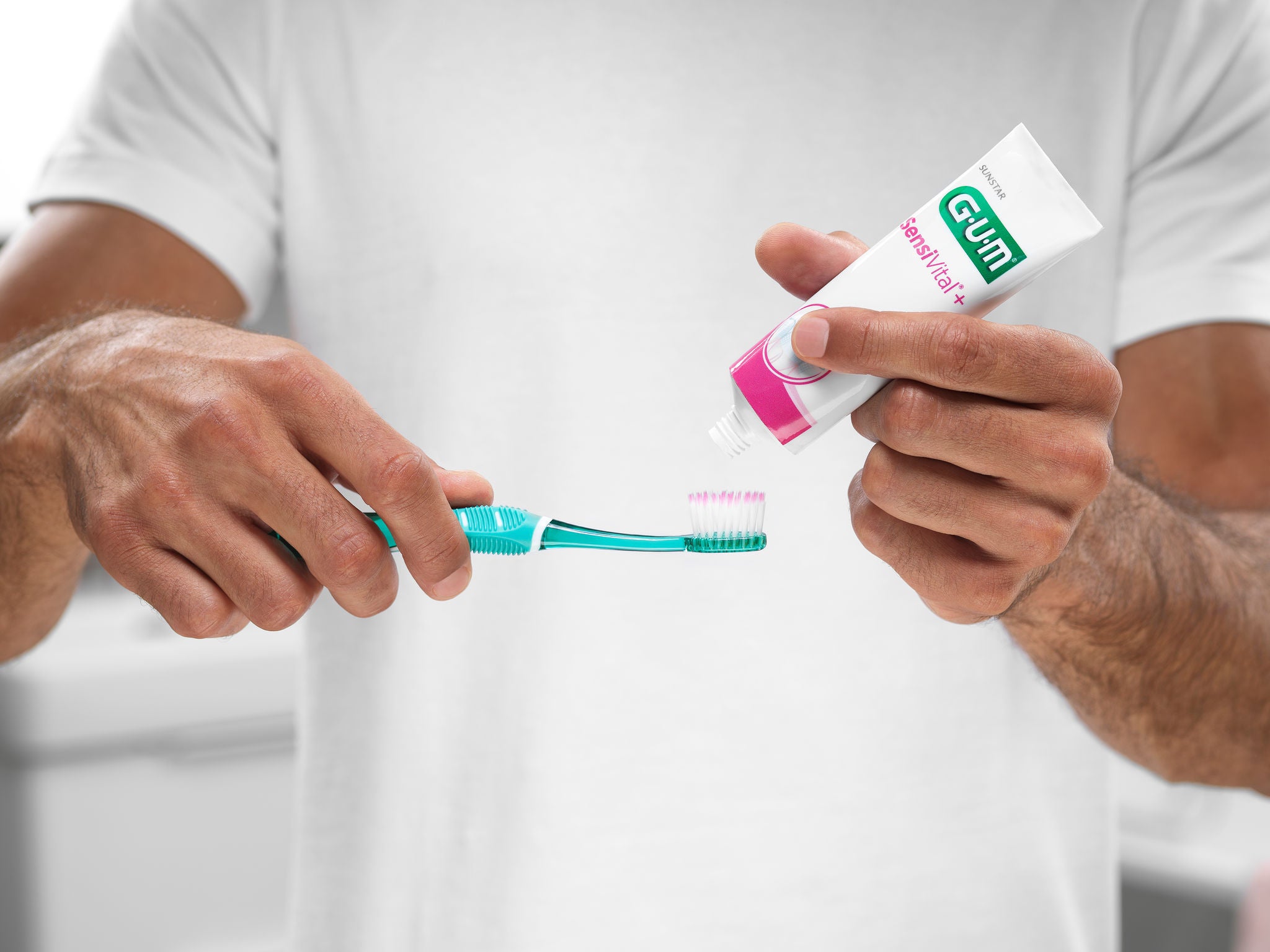 Man is putting the GUM SensiVital+ toothpaste on the GUM PRO SENSITIVE toothbrush to start brushing his teeth