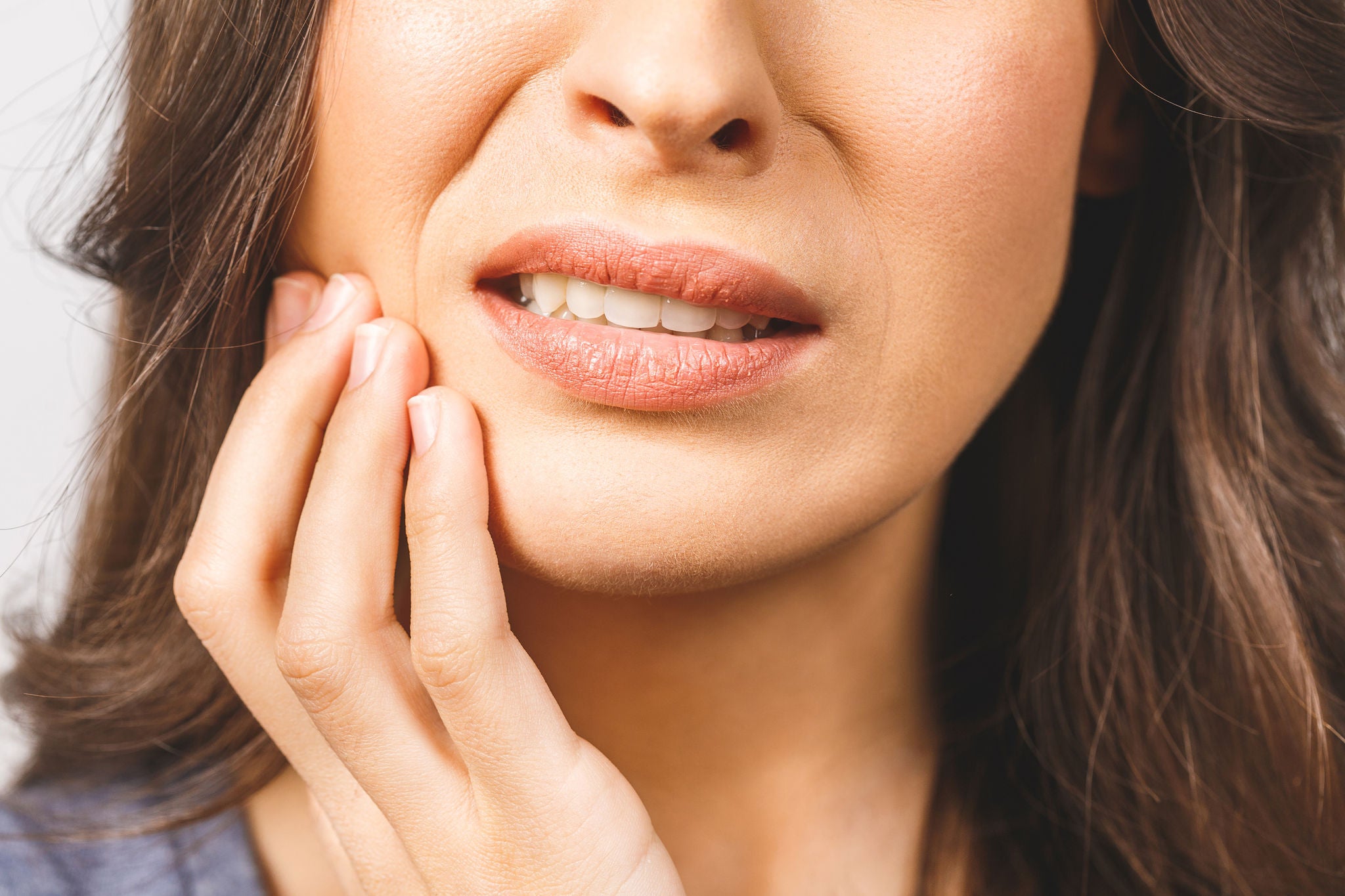 Young European woman isolated on white background suffering from severe toothache, feeling pain so strong that she is pressing fingers to cheek to calm it down, looking desperate.