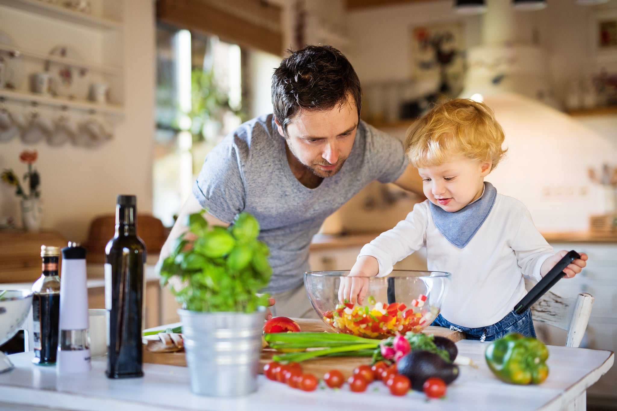 Father with toddler in kitchen cooking. Vegetables salad