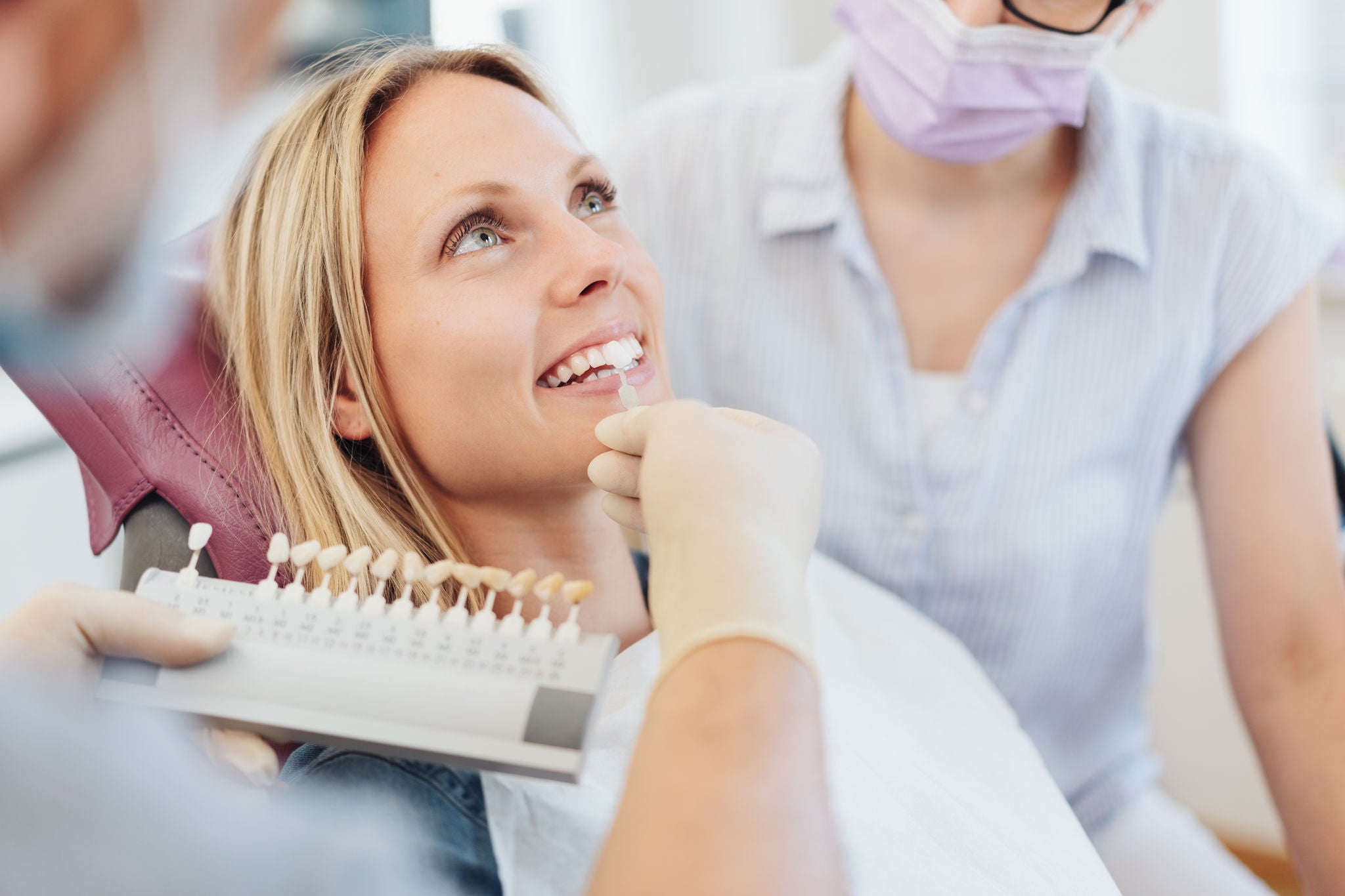 Dentist checking the whiteness of a patients teeth against color coded samples during an examination in his surgery