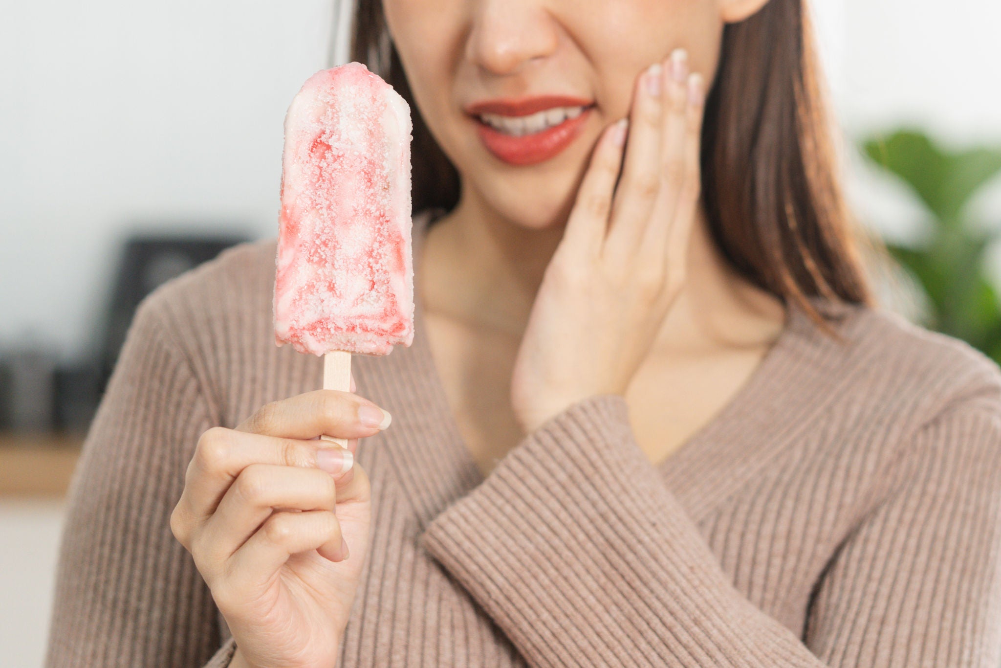 Face expression suffering from sensitive teeth and cold, asian young woman, girl hand holding,  eating ice cream, touching her cheek, feeling hurt, pain. Toothache molar tooth at home, dental problem.