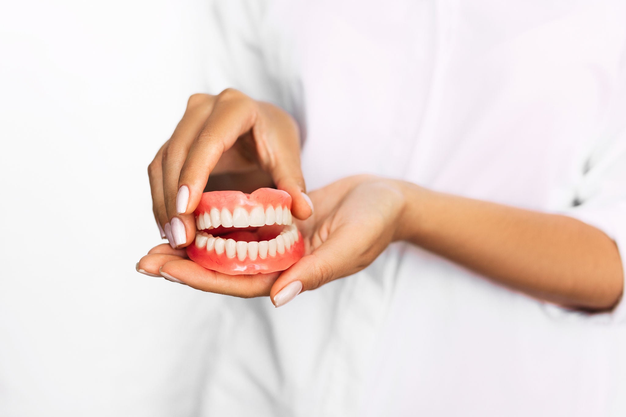 Dental prosthesis in the hands of the doctor close-up. Dentist holding ceramic dental bridge. Front view of complete denture. Dentistry conceptual photo. Prosthetic dentistry. False teeth