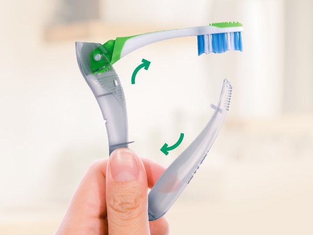 Hand holding the folded GUM TRAVEL toothbrush