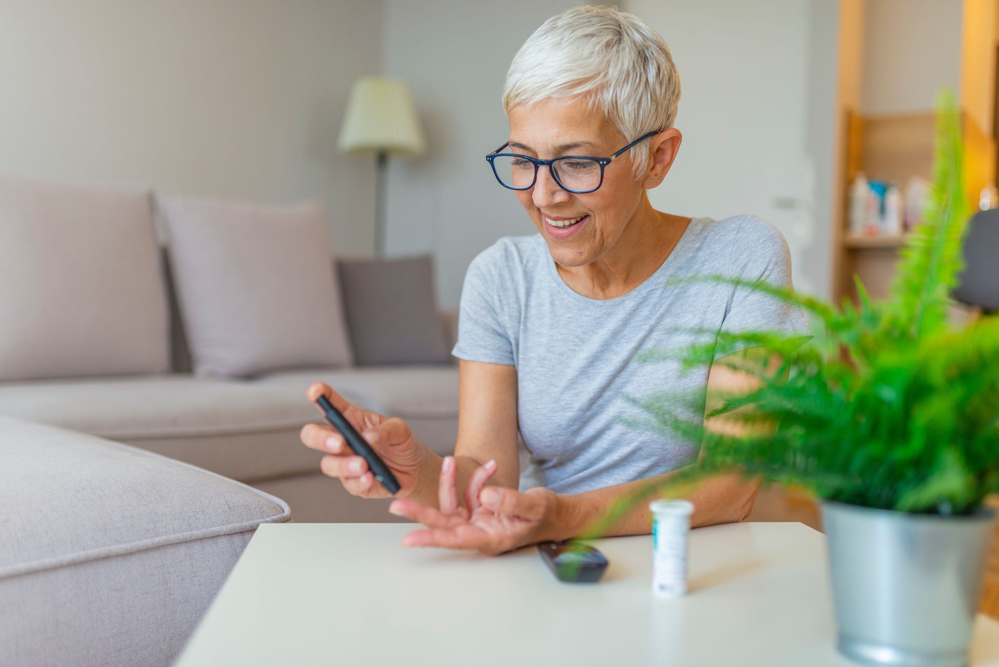 Happy mature woman with glucometer checking blood sugar level at home. Woman testing for high blood sugar. Woman holding device for measuring blood sugar