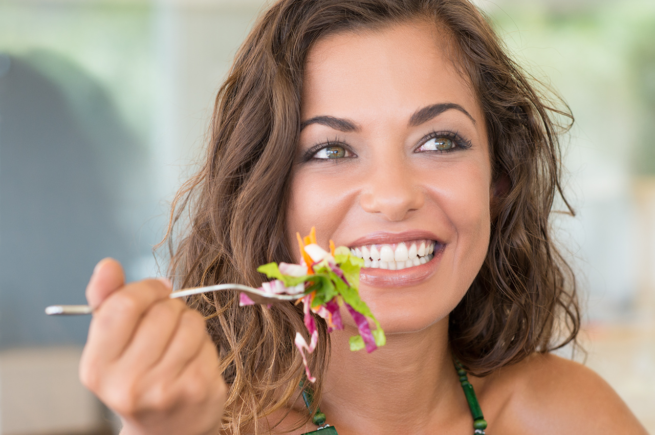Smiling woman eating salad with fork in hand