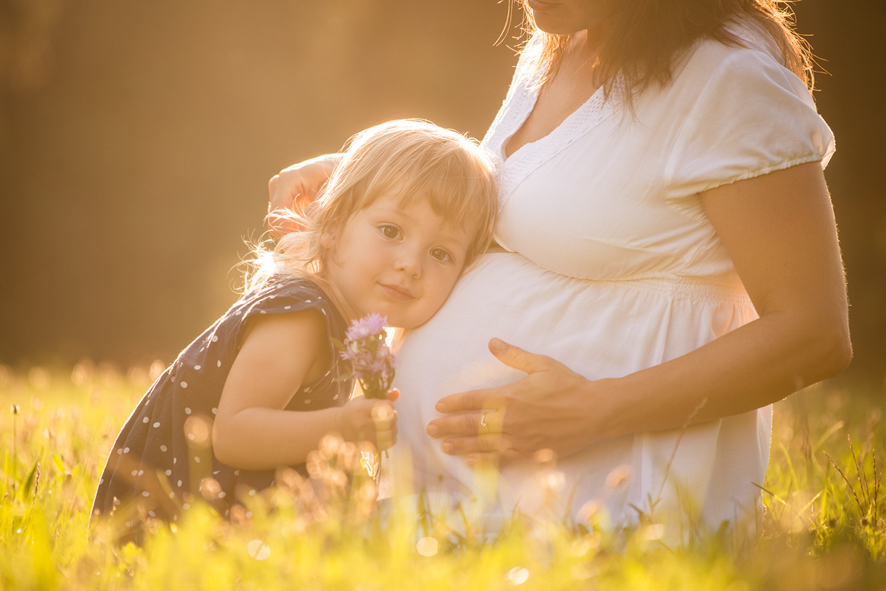 Little child listening baby in belly of her mother outdoor in sunny nature outside