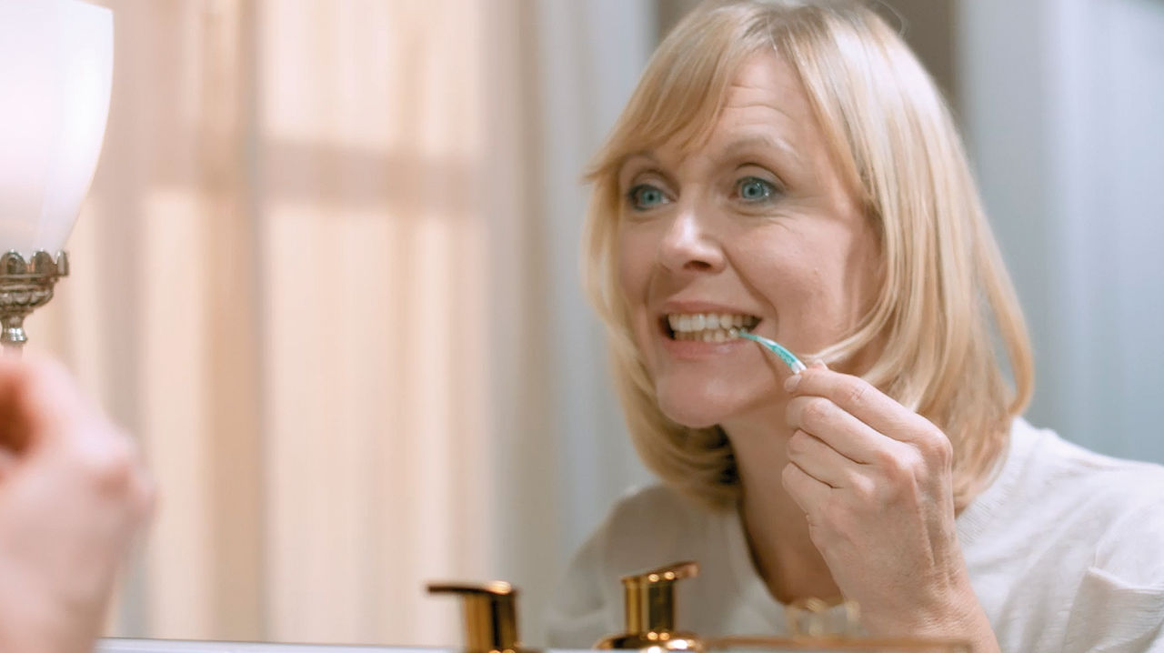 Ein lächelnder Mann verwendet einen Gummi-Interdentalreiniger, um seine Zahnzwischenräume zu reinigen