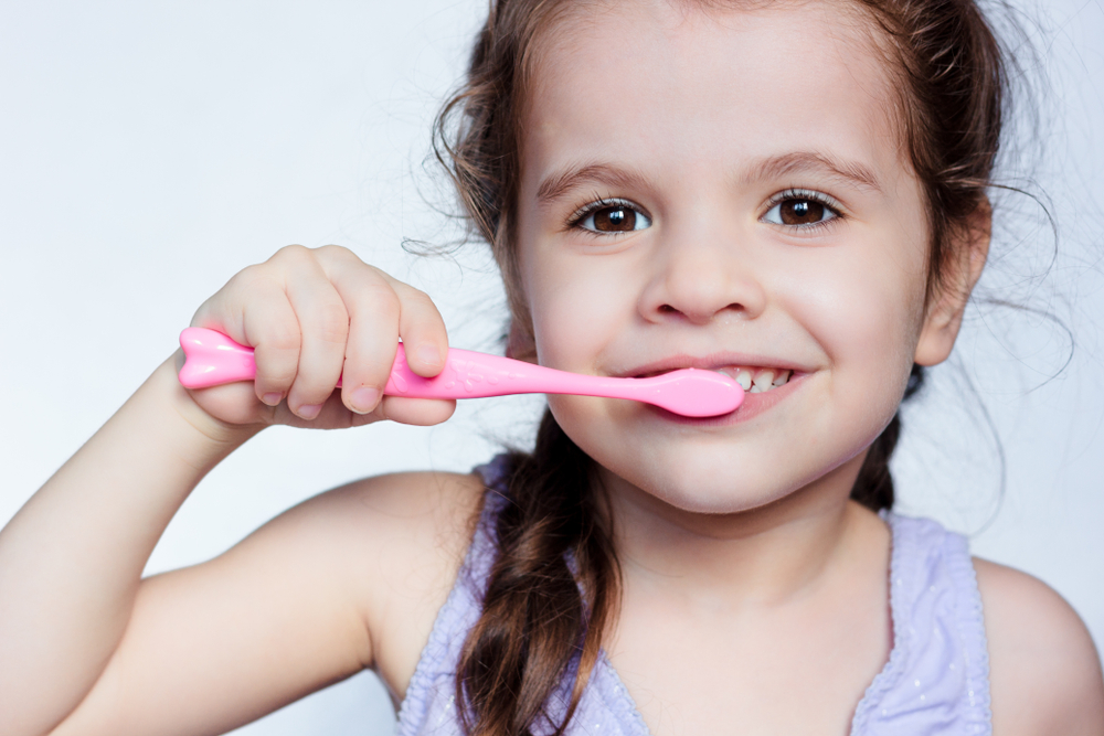 Small girl brushing teeth with pink toothbrush