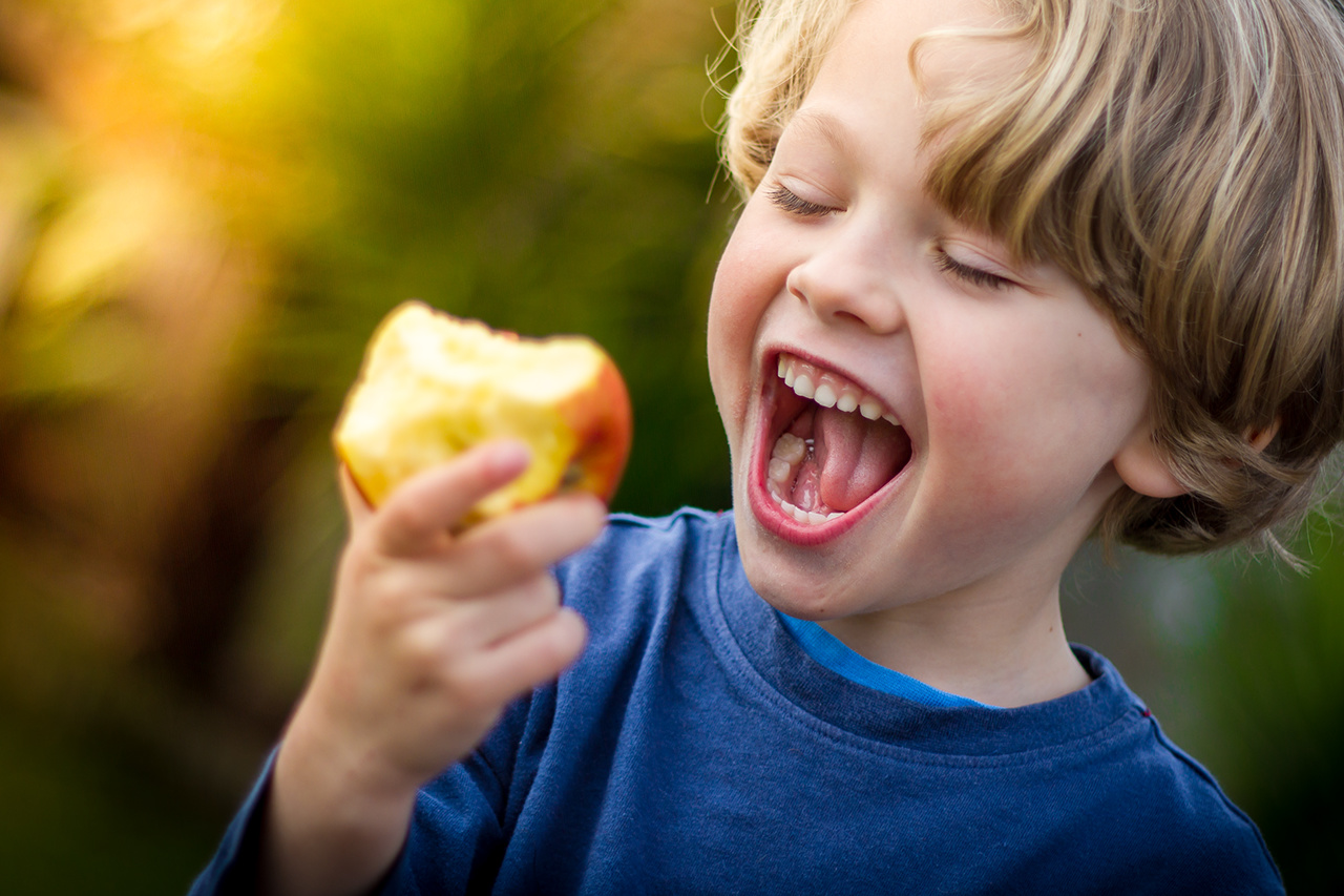 Child boy with mouth open about to take a bite of an apple outdoor