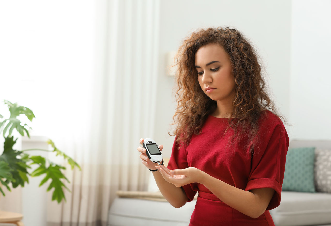 Young African-American woman using digital glucometer at home. Diabetes control