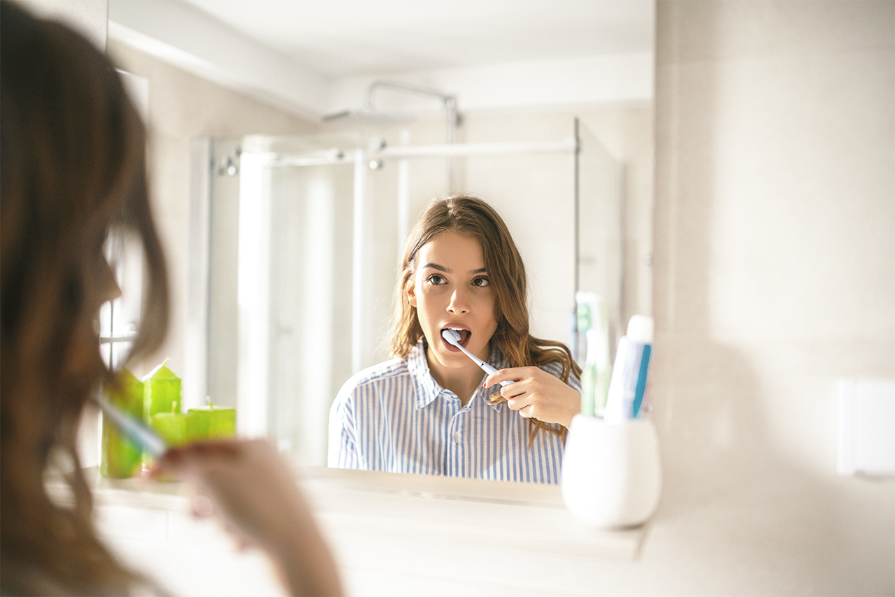 Woman brushing her teeth with a GUM ActiVital Sonic toothbrush bathroom mirror