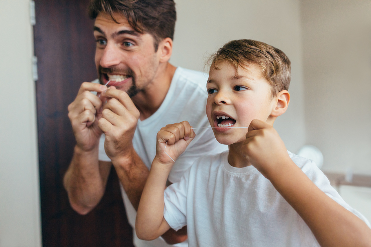 Boy kid with father male man in bathroom cleaning teeth with dental floss