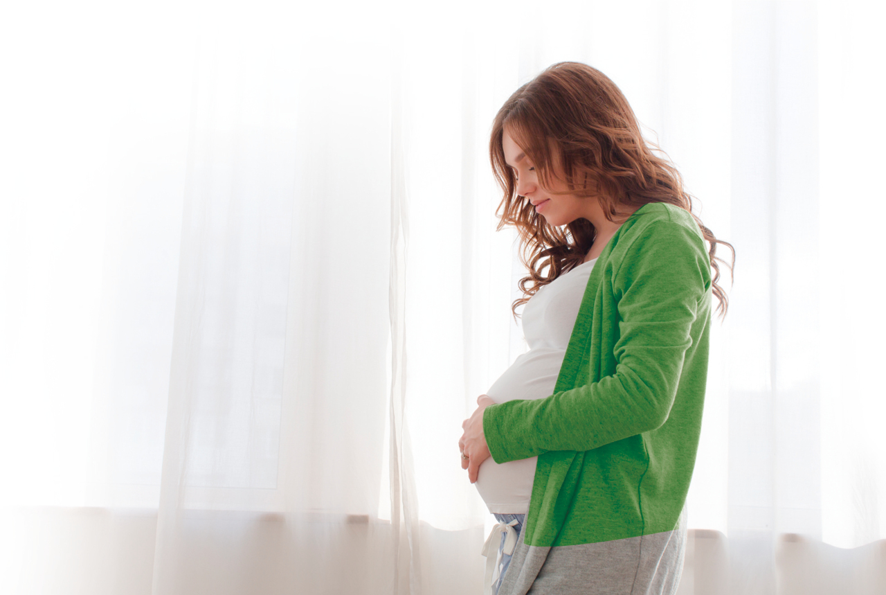 Pregnant female woman with light green shirt eating cereal in kitchen
