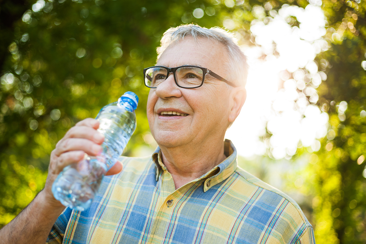 Older man male is drinking water outside in park